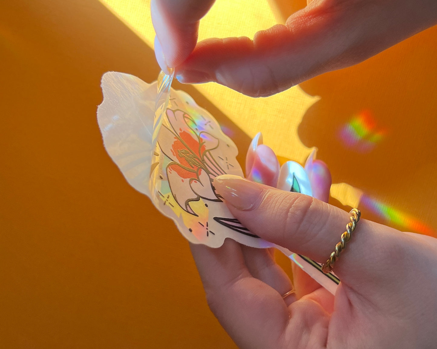 Hand unpeeling the lily suncatcher window sticker from the protective backing.