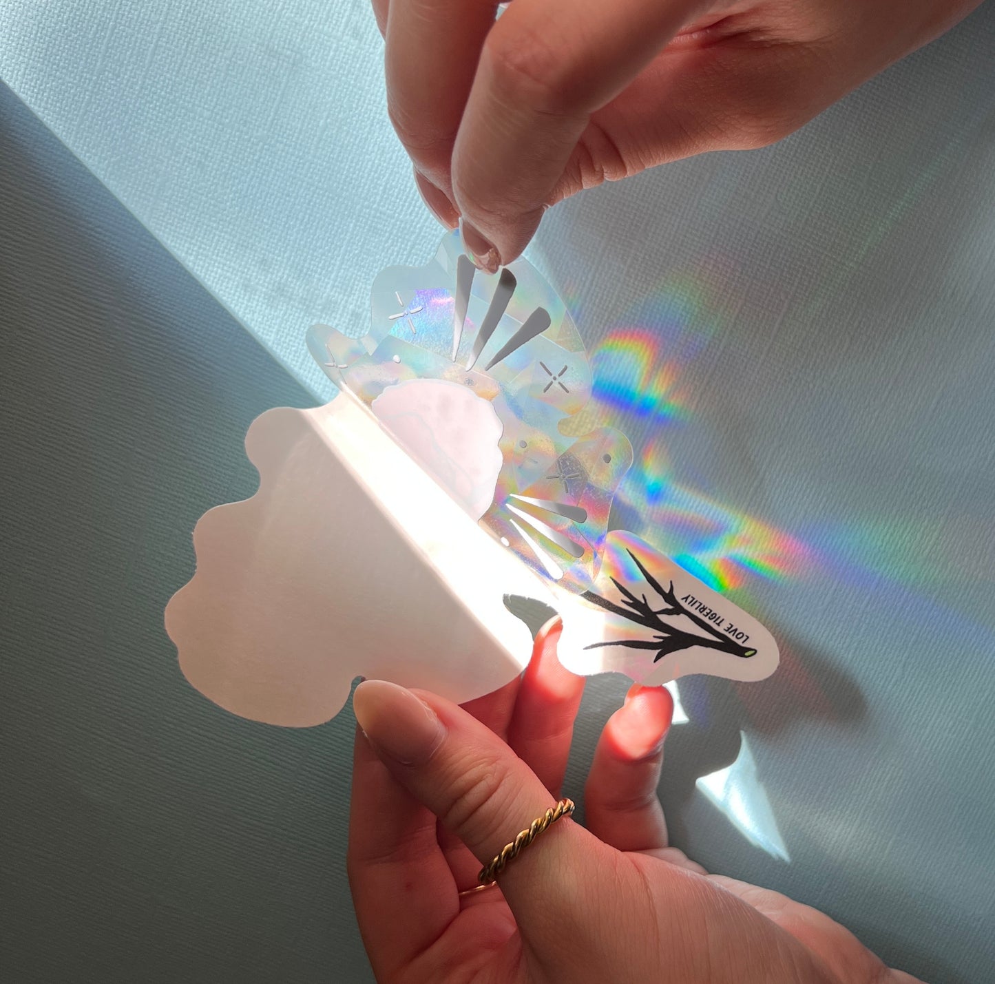Hand unpeeling the California Poppy suncatcher window sticker from the protective backing.