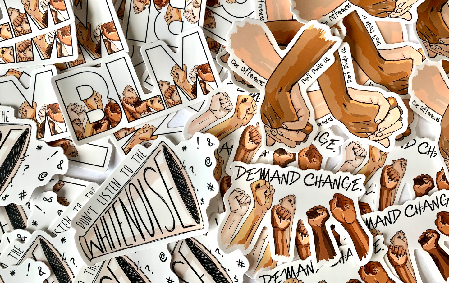 Picture featuring 4 different stickers in support of the Black Lives Matter Movements. Top Left corner sticker has the letters BLM with fisted hands. Top Right Sticker has holding hands with words around them saying our difference doesn't divide us. The bottom left sticker has a blow horn saying don't listen to the white noise. Bottom right says demand change with fists raised. All sticker profit from these 4 stickers will be donated to black organizations.