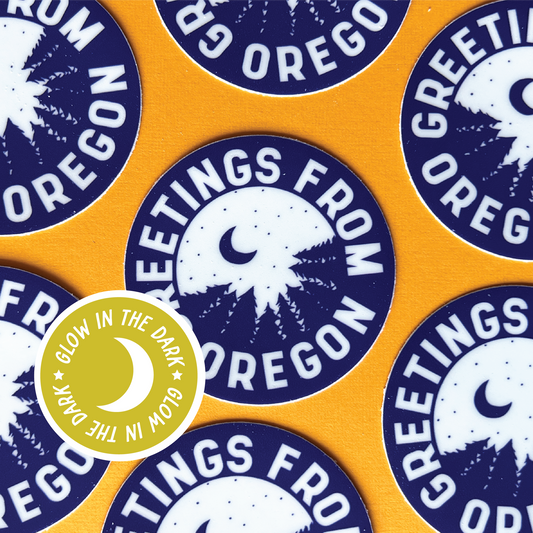 Round glow in the dark sticker that has a blue outdoor forest scene with the stars and moon surrounded by text that says greetings from oregon.