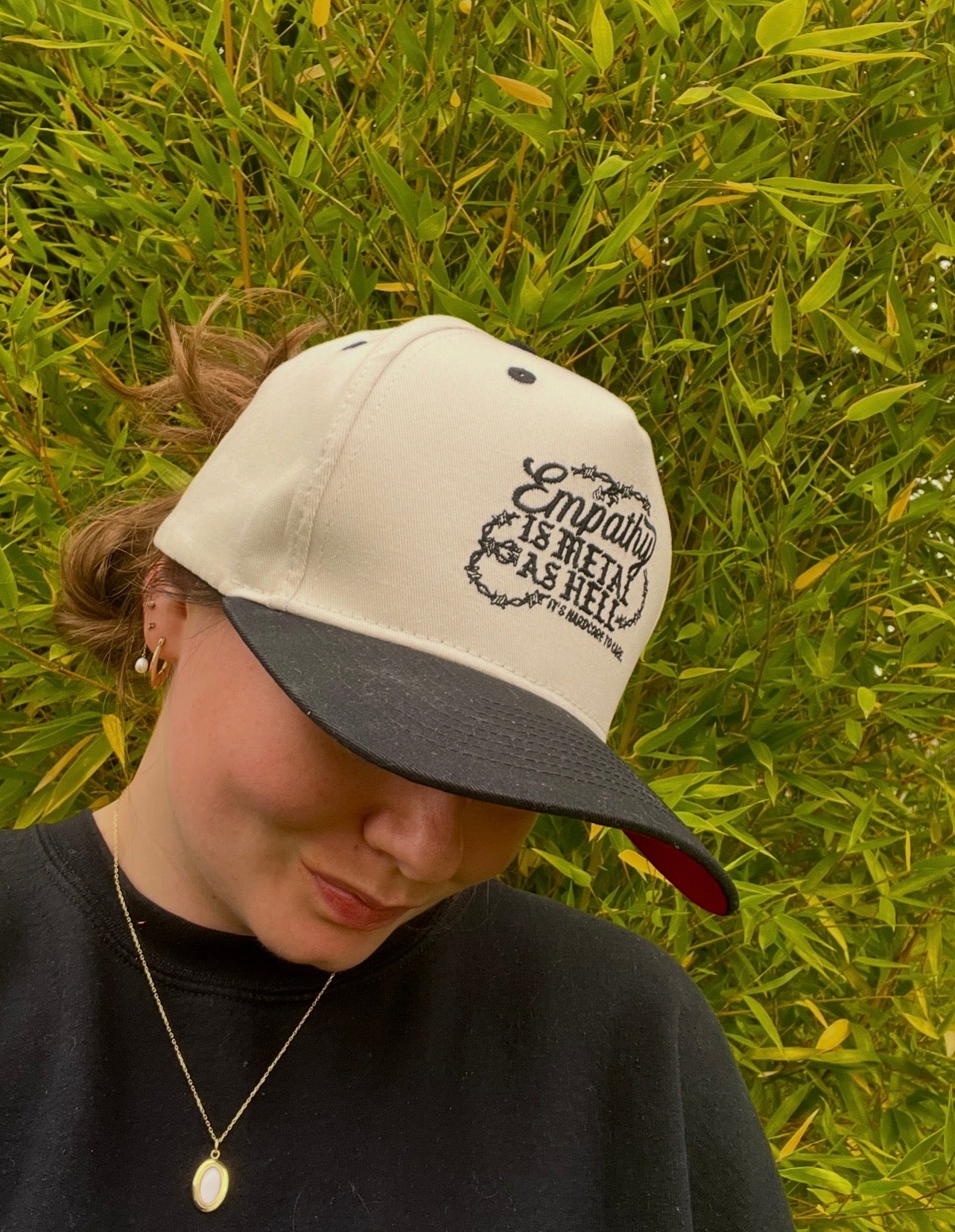 Person wearing a cap that says empathy is metal as hell in a grassy field
