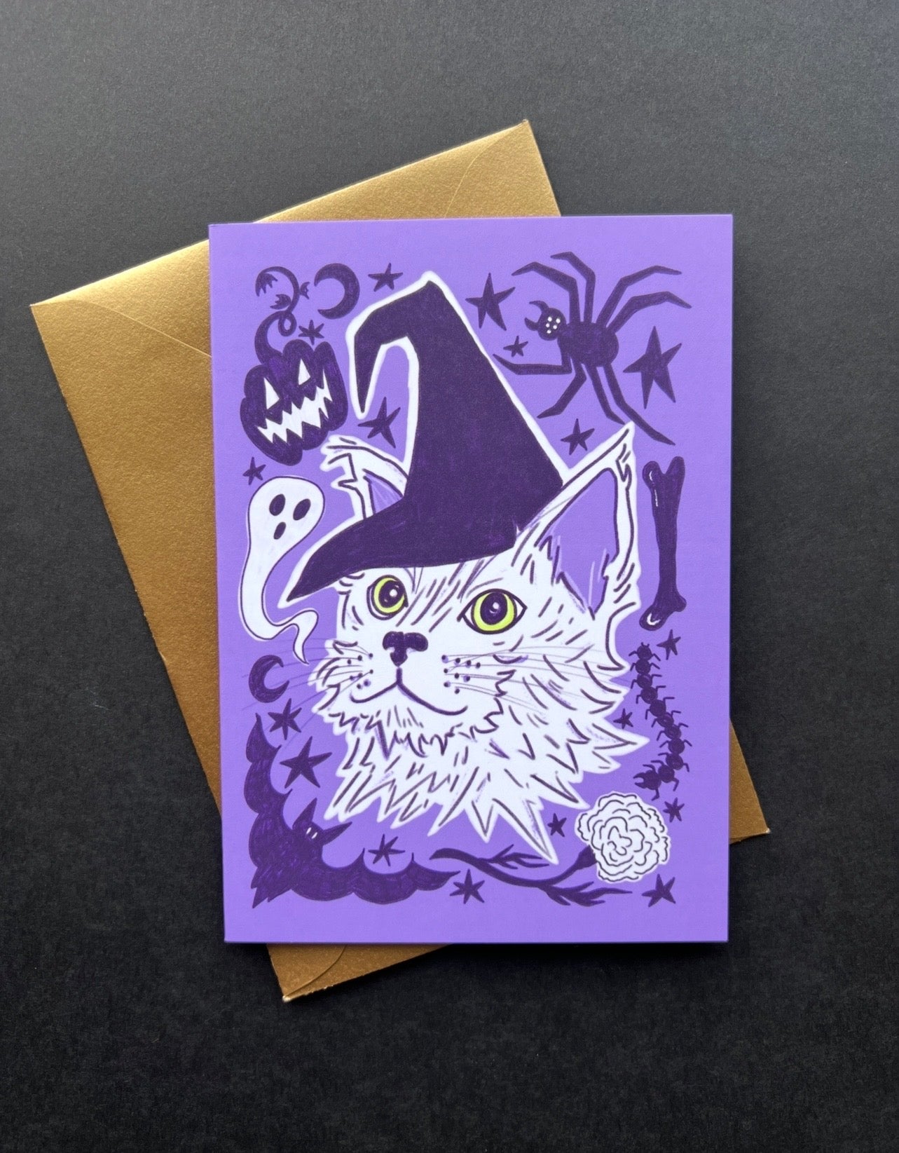 Halloween-themed card with a cat wearing a witch hat on a purple background, featuring pumpkins, ghosts, and spiders.