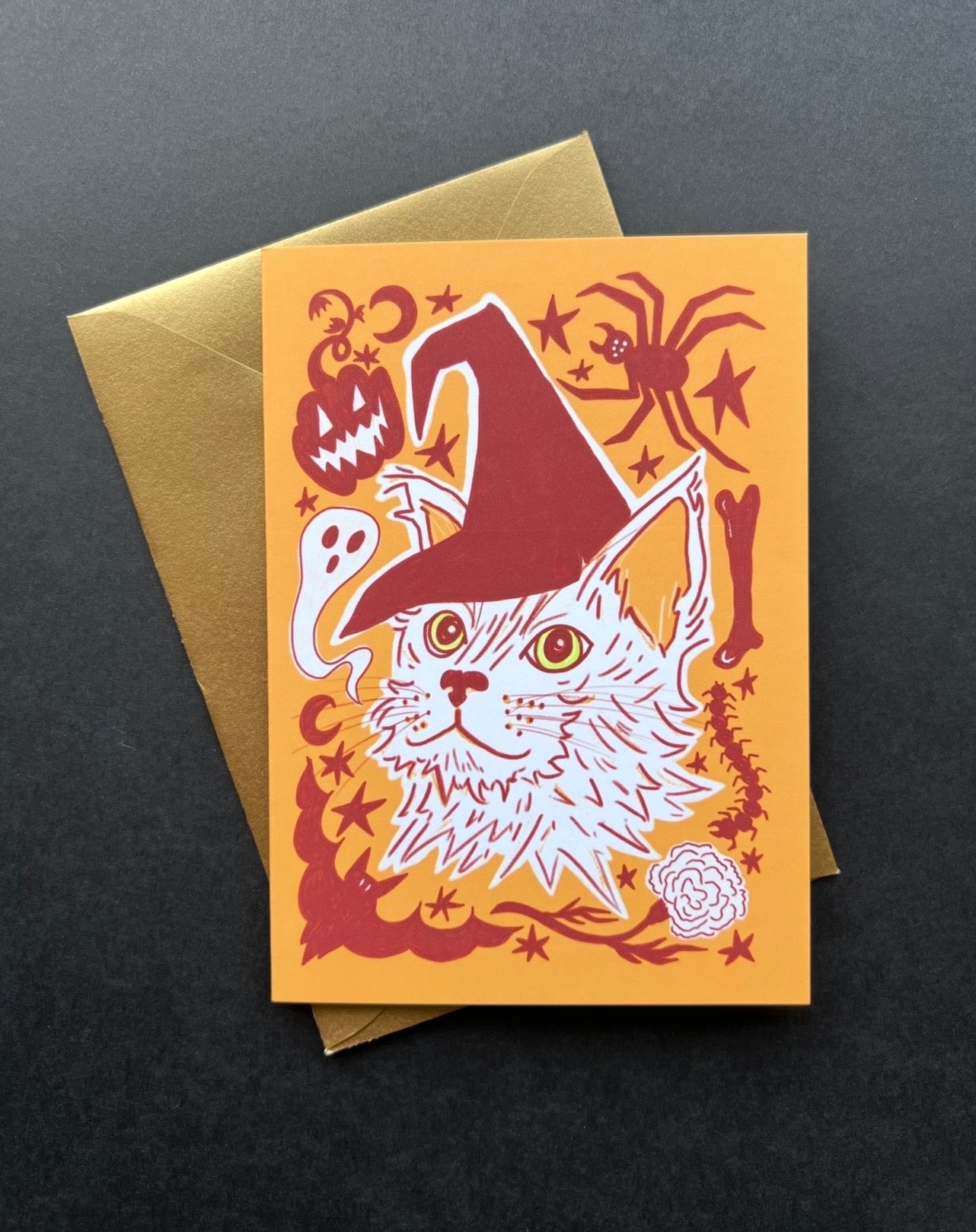 Halloween-themed card with a cat wearing a witch hat and gold envelope on a black background