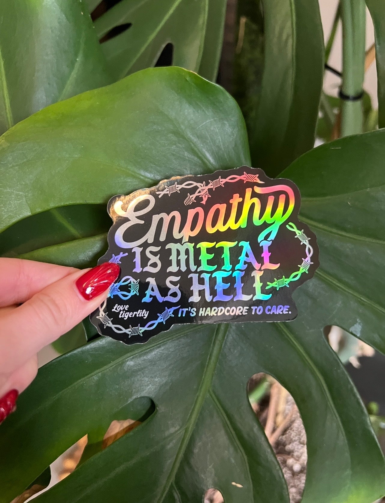 Holographic stickers with 'Empathy is metal as hell & it's hardcore to care' text design with barbed wire held by a monstera plant