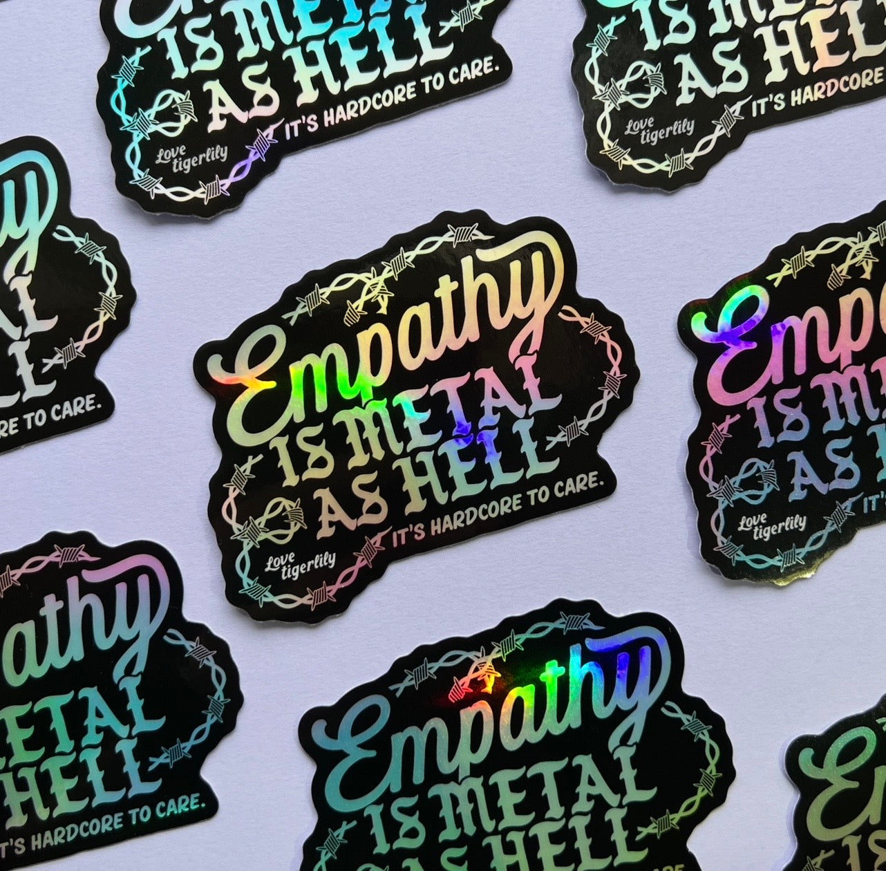 Holographic stickers with 'Empathy is metal as hell & it's hardcore to care' text design with barbed wire on a light purple background