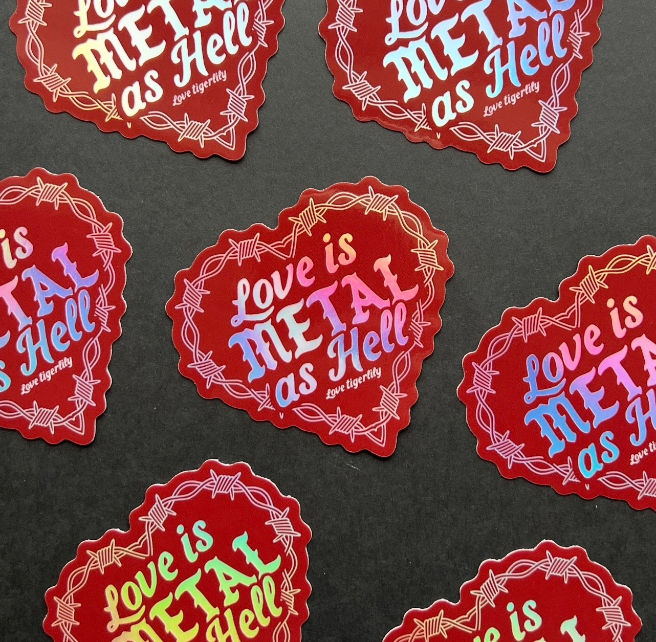 Red Holographic heart stickers with 'Love is metal as hell ' text design with barbed wire on a black background