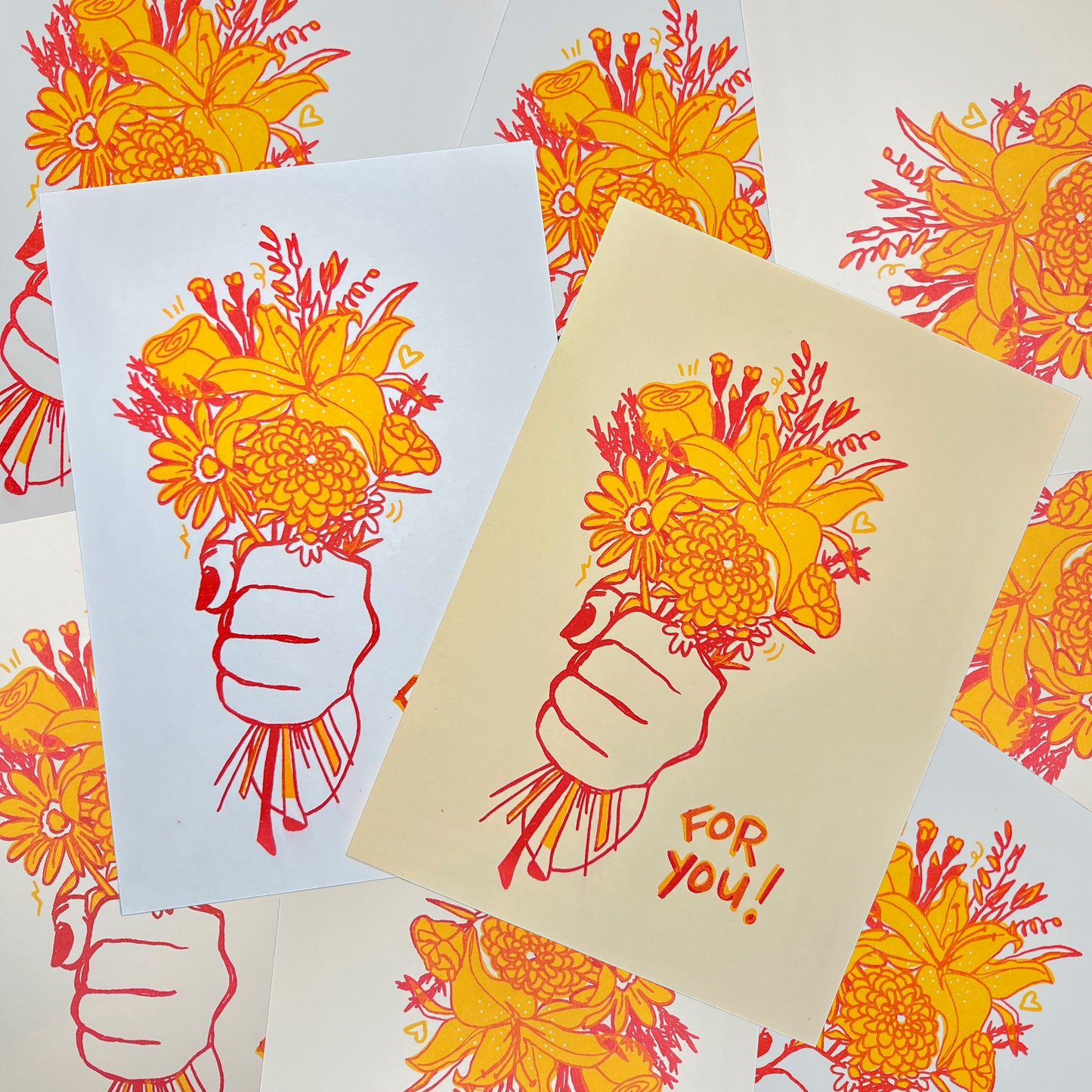 Photo showing the “For You” hand illustrated riso print of a bouquet of flowers in a fist with red and yellow risograph ink on both white and tan colored paper.