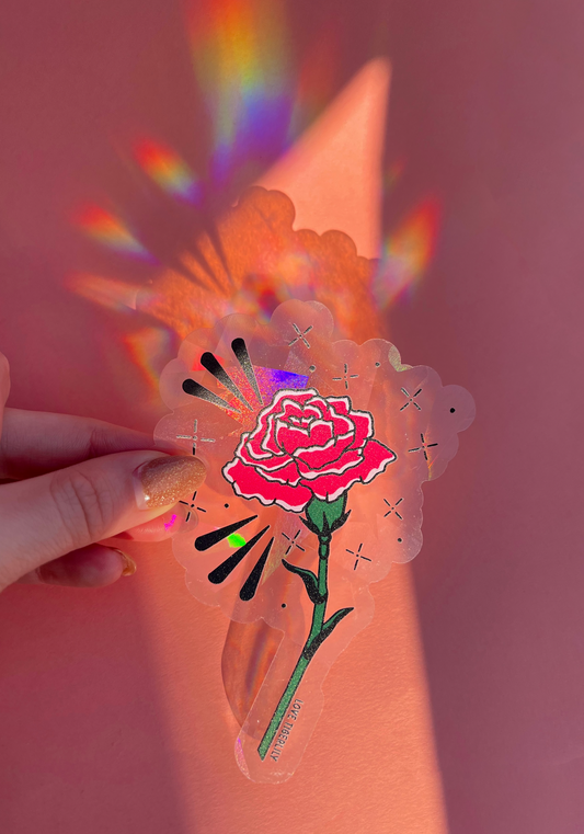 Hand holding the pink carnation suncatcher window sticker over a pink background so that it casts rainbows.